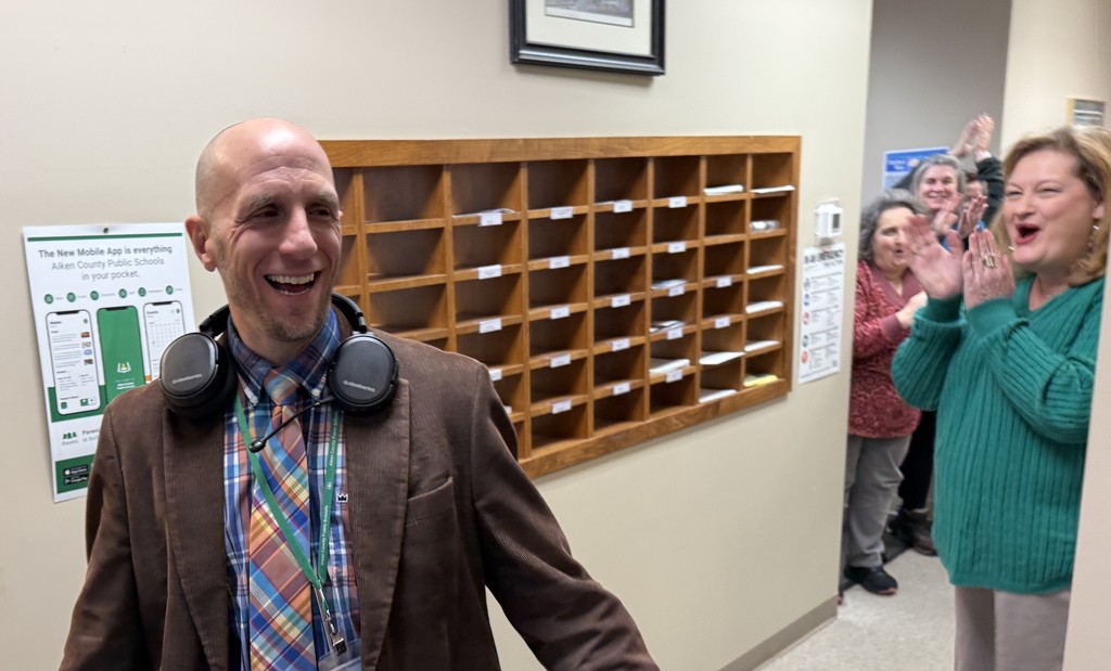 A man smiles as a hallway of people clap.