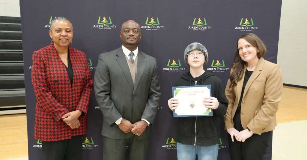 Student holding commemorative certificate with school administrators 