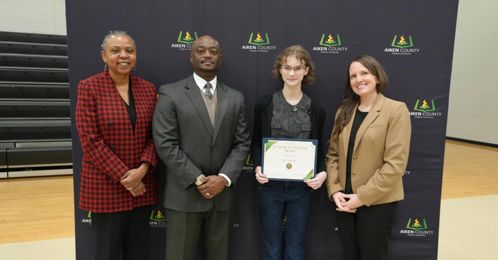 Student holding commemorative certificate with school administrators 