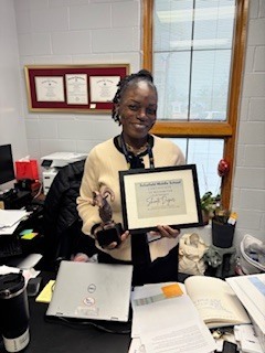 A lady standing in her office holding a certificate.