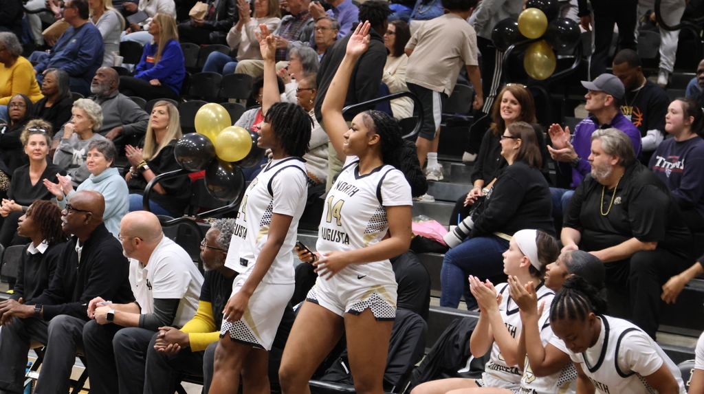 2 Girl basketball players cheering with fans in background.