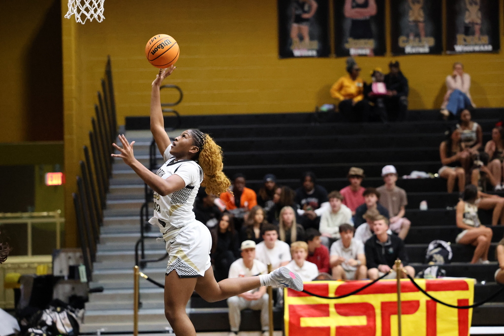 Girl basketball player making a layup with fans in bleachers.