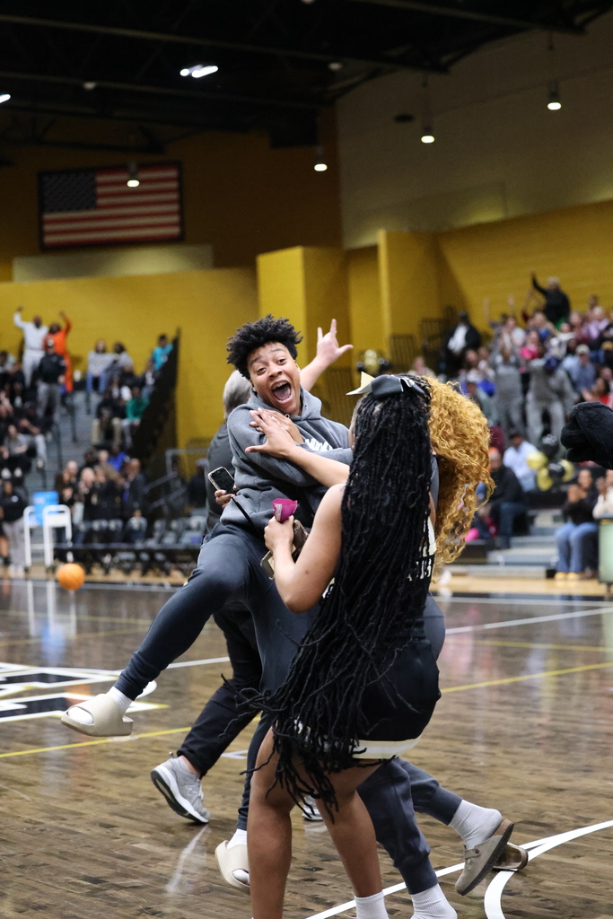 Girls jumping and celebrating with other students in gym with people on bleachers.