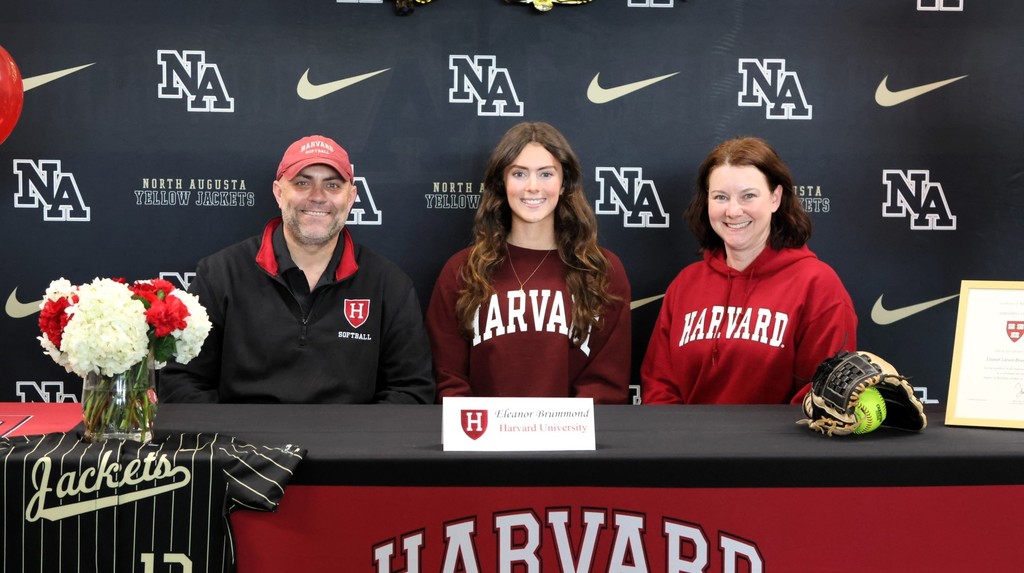 Female student sitting at desk with parents for Harvard University Signing. 