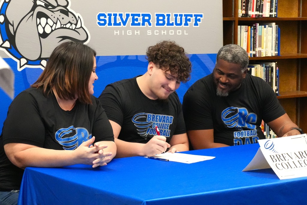 Adrian Gray signs NCAA Letter of Intent sitting in between his parents to play football at Brevard College in the fall.