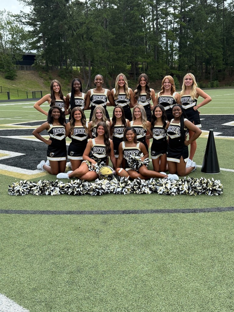NAHS cheerleaders posing on football field with line of pompoms in front.
