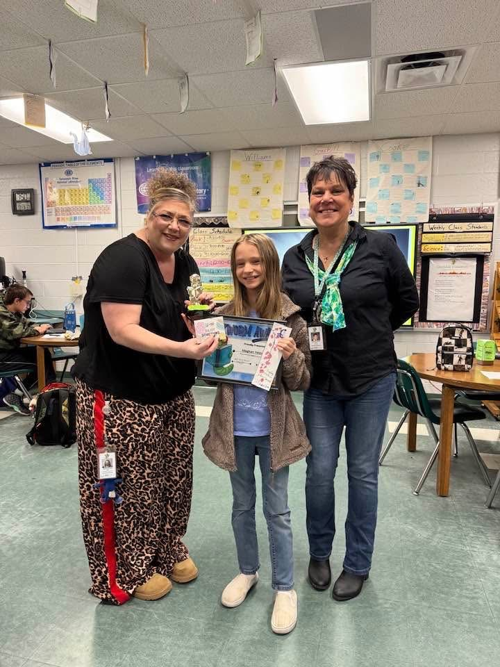 Student standing with adults getting her award for bookmark contest