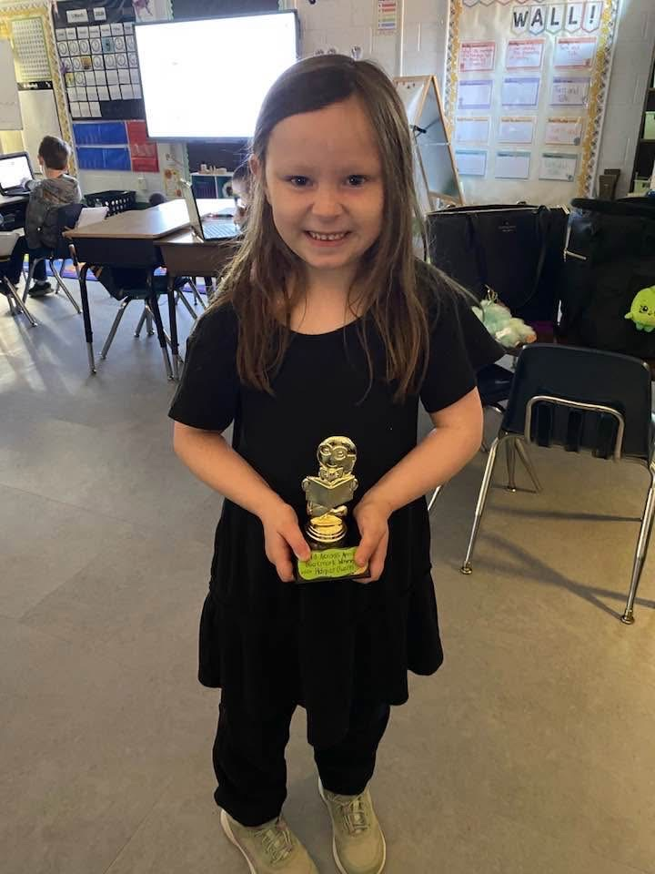 student holding her bookmark contest trophy