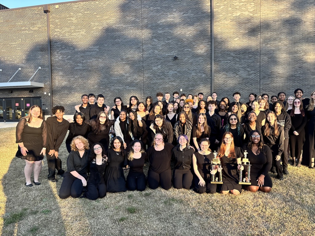NAHS Orchestra posed outside with trophies.