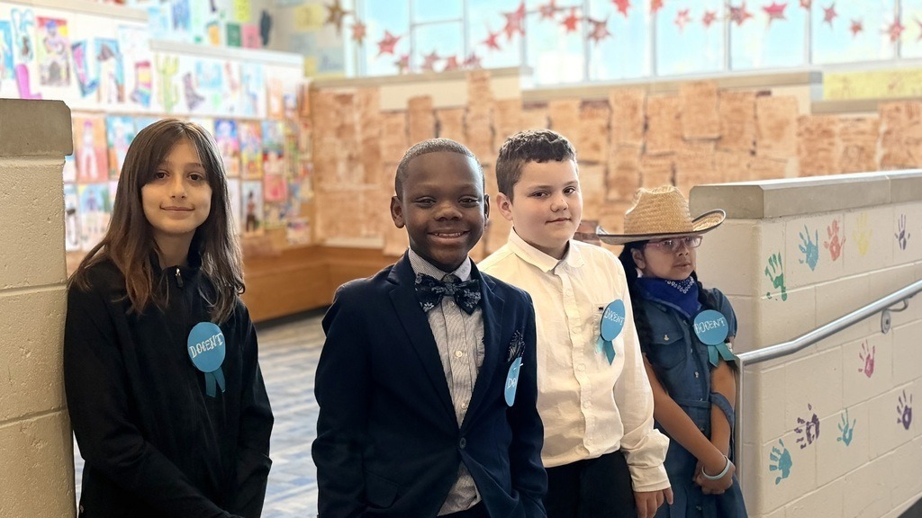 Four elementary students standing in front of art wall.