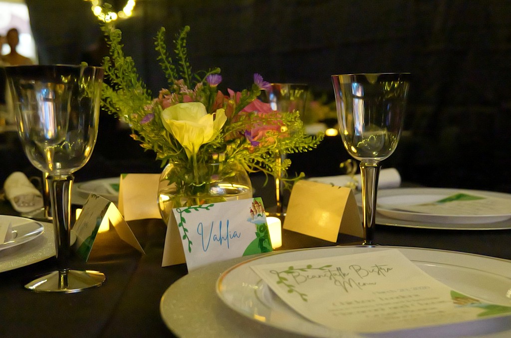 Name plates and floral arrangements are set up on student tables with menus.