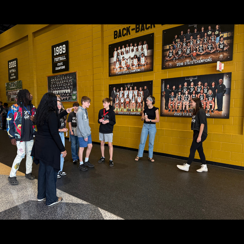 Students standing in front of gym wall talking with state championship posters in background.