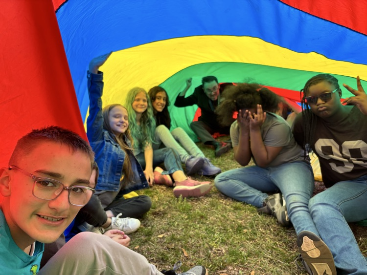 young student girls and boys playing under a parachute for field day