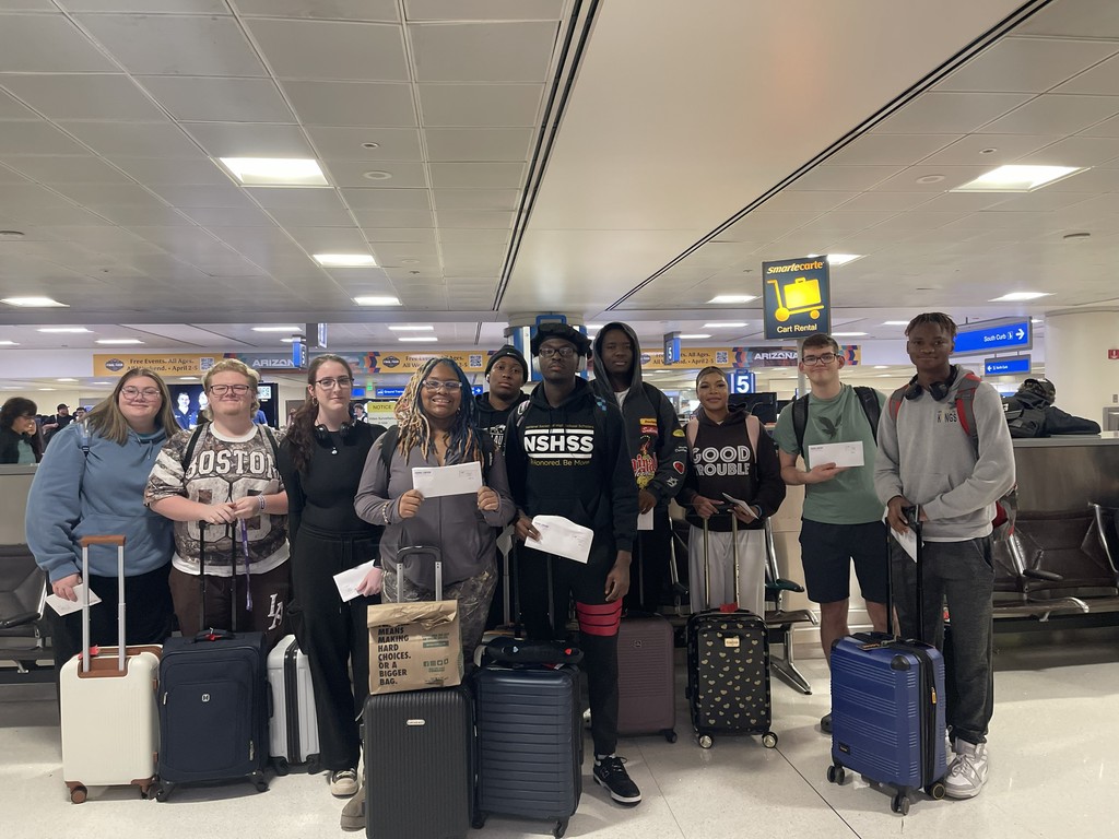Students posing with luggage at airport.