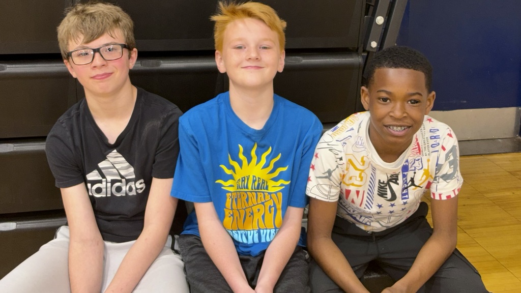 three students posing for a photo in front of bleachers in a gym.