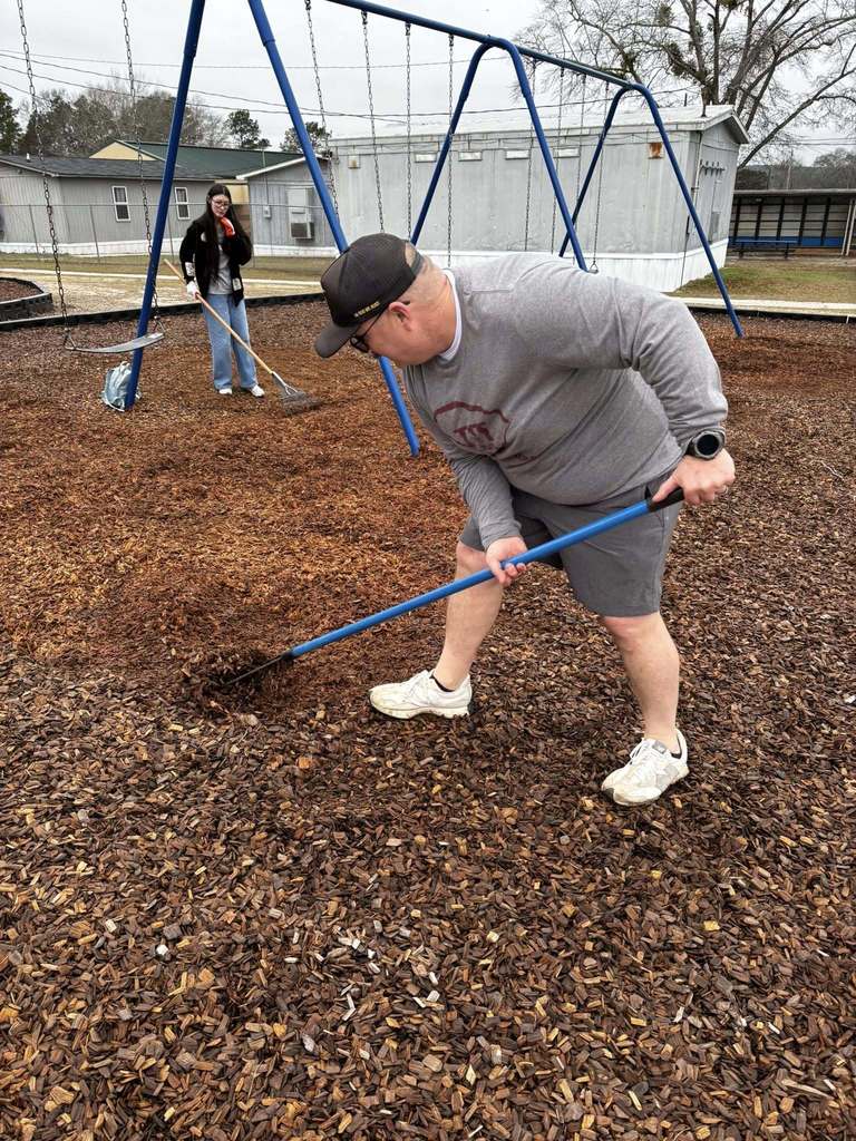 Two volunteers raking the playground wood chips.