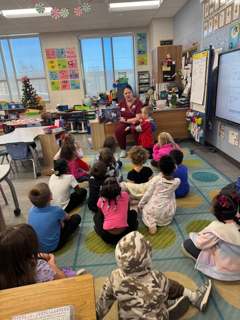 Group of students sitting on classroom floor listening to volunteer read a book.