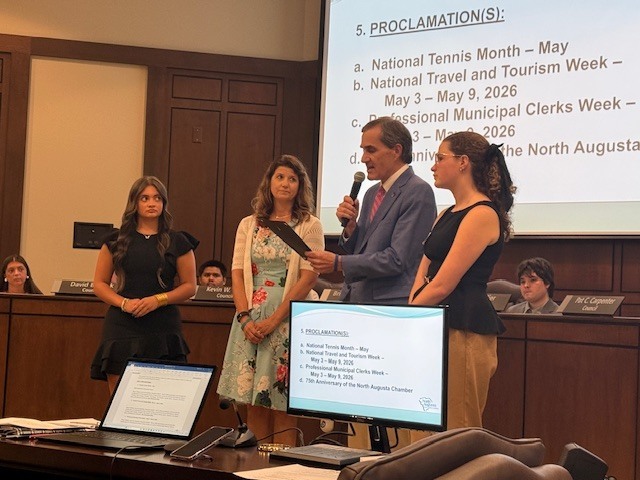 Mayor speaking with students behind mayor in council chamber. 