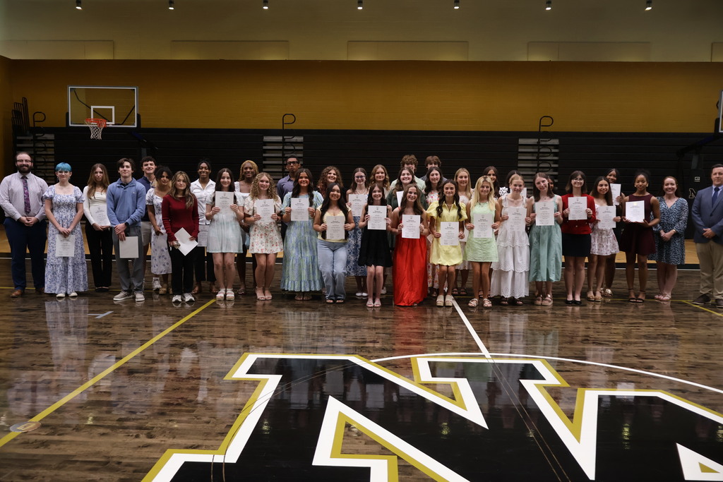 Students in gym holding up NHS certificates with part of NA logo on floor.