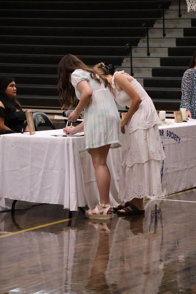 2 girls at table signing book. 