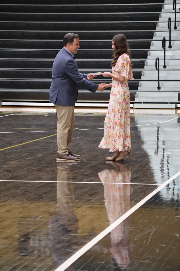 Girls shaking principles hand in gym. 
