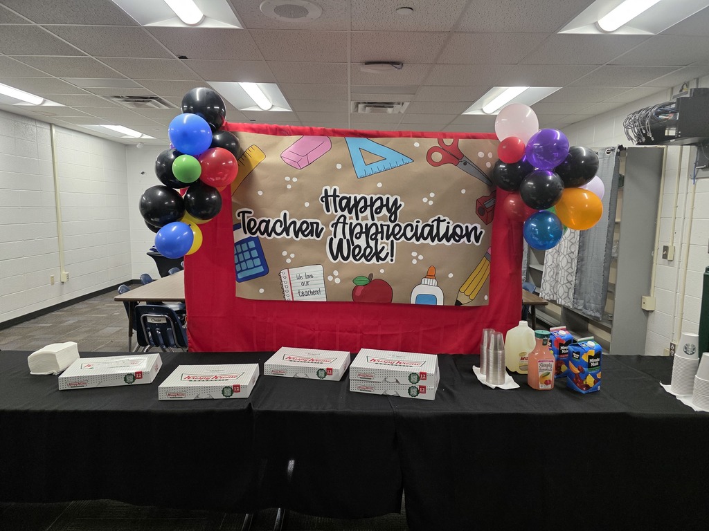 Boxes of donuts and bottles of juice on table in front of banner hat syas Happy teacher Appreciation Week.