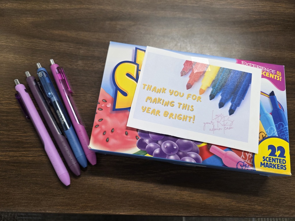 Box of markers and four pens on table.
