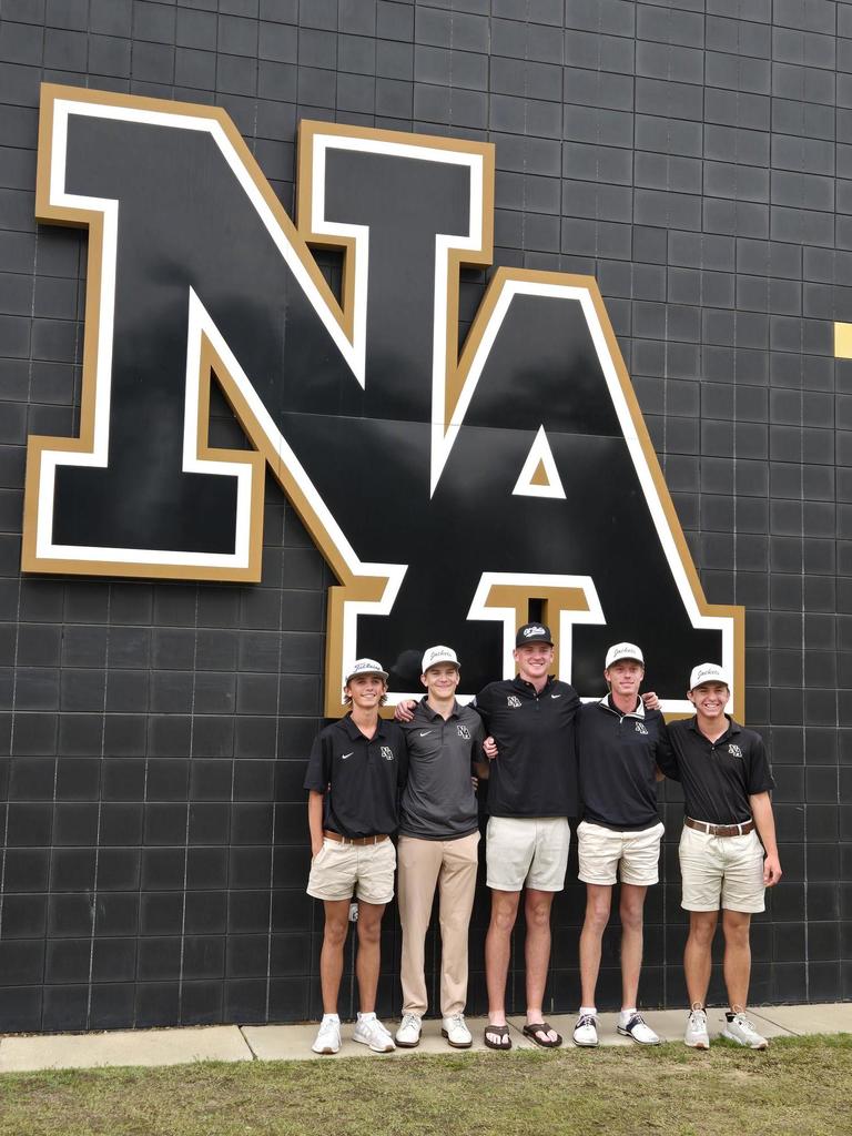Golf team in front of wall with NA logo. 