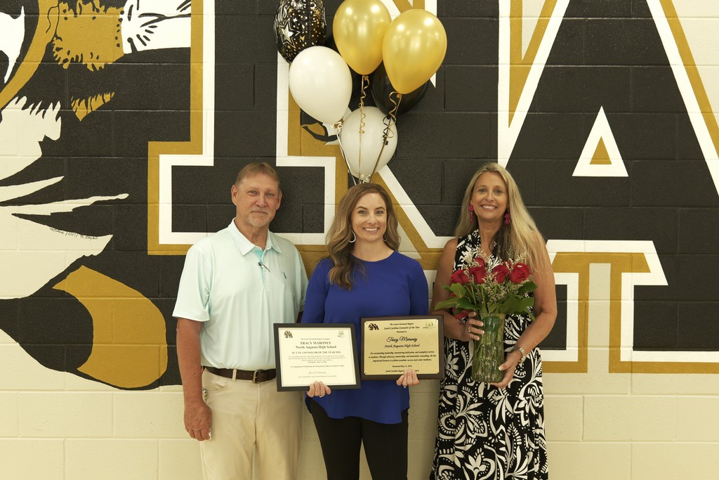Tracy poses with two staff members shocasing her awards and recognition.