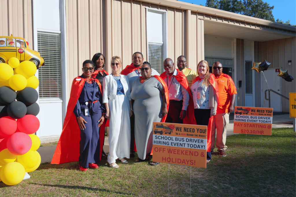 Transportation department staff standing in front of office while wearing red capes.