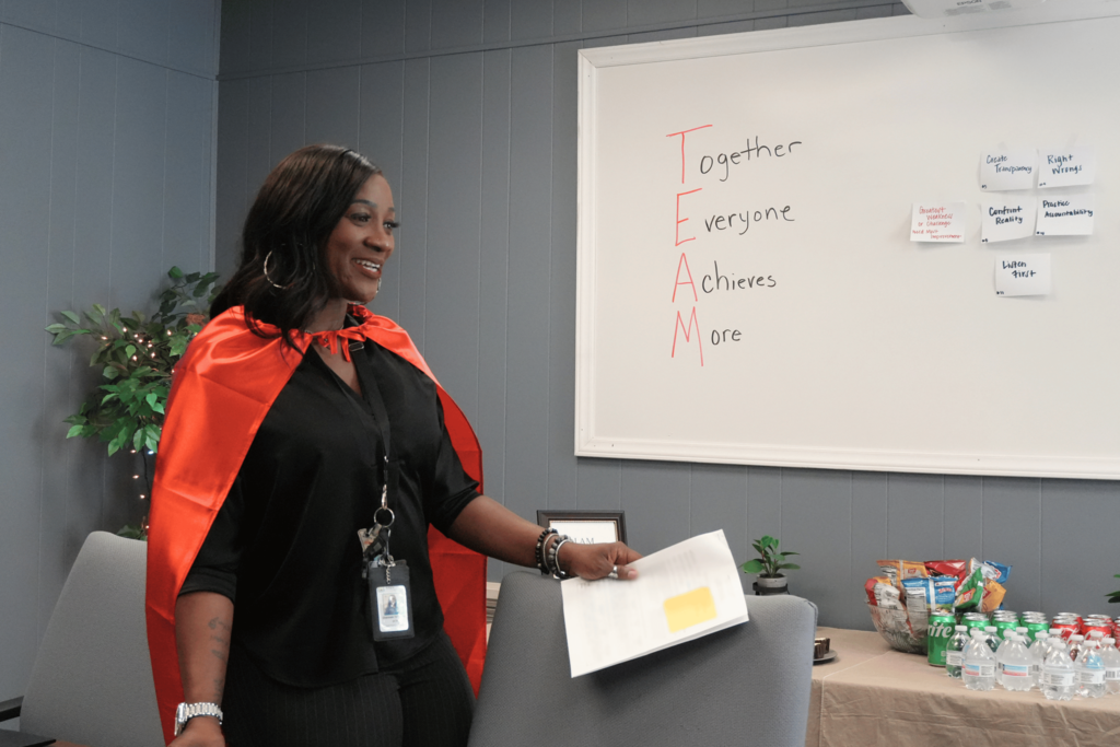 Transportation employee smiling in front of white board with TEAM acronym.