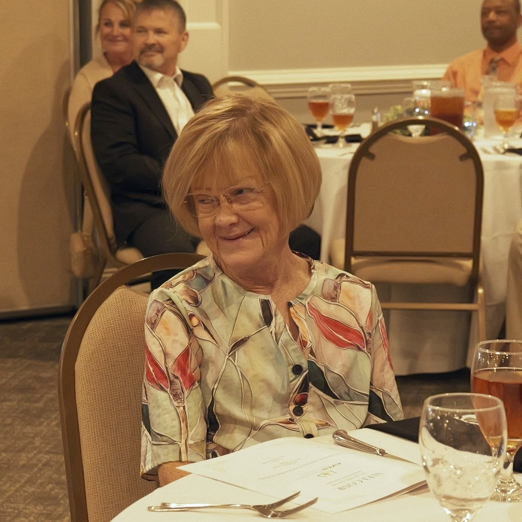Woman is sitting and smiling at a table during a retirement banquet. 