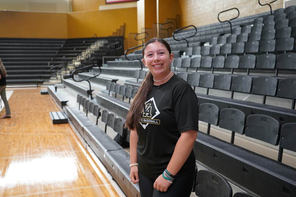Student smiling in gym with bleachers in the background. 