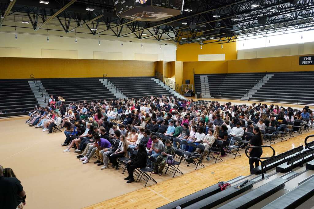 Students sitting in a gym in chairs. 