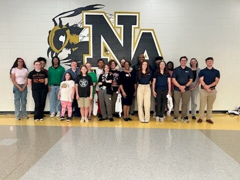 Students and teachers and mentors posing in front of NAHS Jacket Logo. 