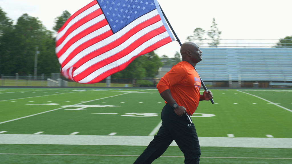Superintendent Corey Murphy running and holding a flag on a track at Midland Valley High School.