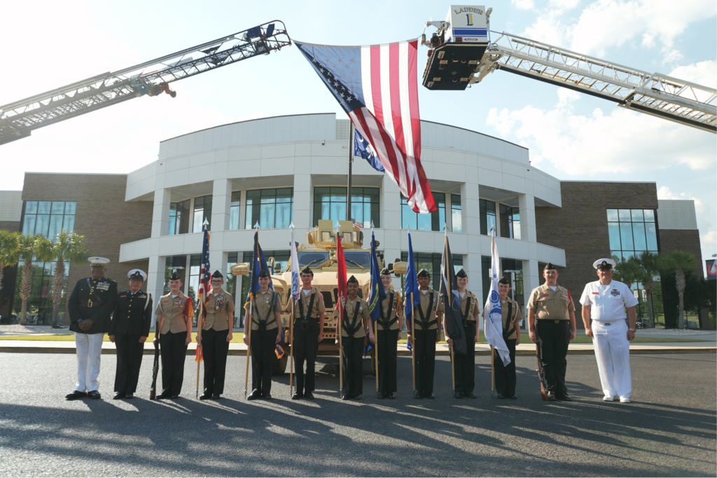 South Aiken High School ROTC posed in front of large American flag whilst carrying the flags of our military.