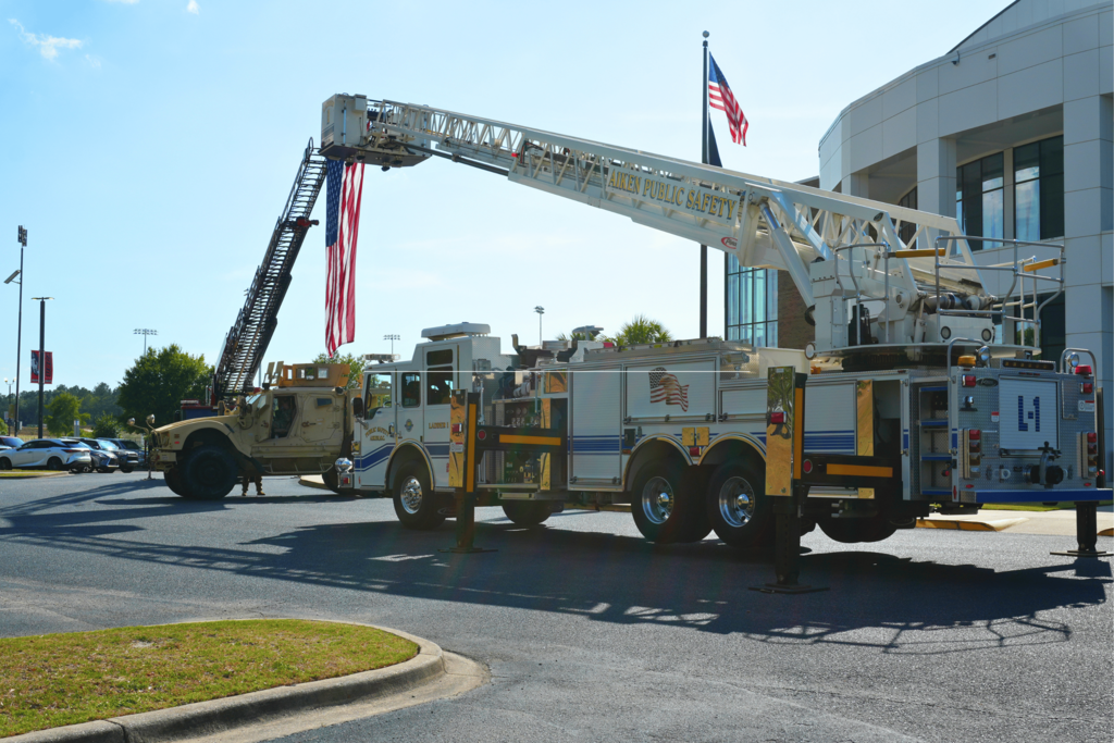 Two public safety trucks holding up large American flag.