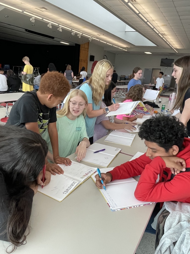 Students at a table talking and signing yearbooks.