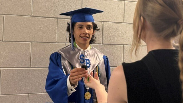 Student graduate standing and speaking to someone prior to their ceremony.