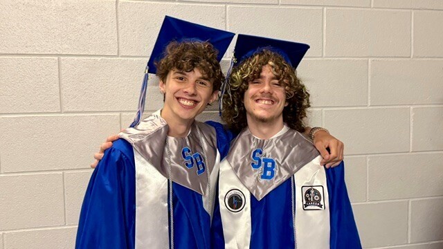 Two male SBHS graduates hugging and smiling before graduation.