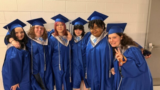 Six graduates posing with smiles and peace signs prior to graduation.