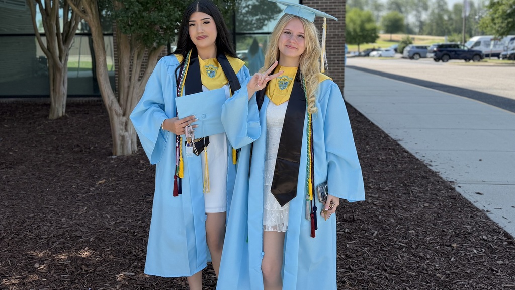 Two students pose outside wearing their caps and gowns before graduation.