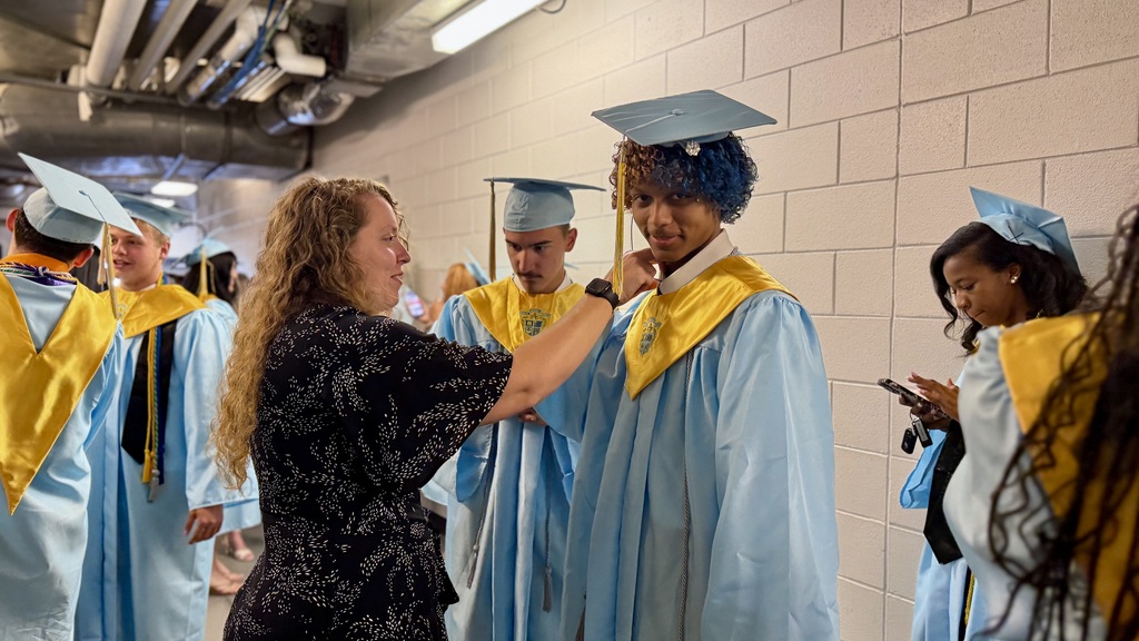 A teacher fixes a graduate's gown prior to graduation.