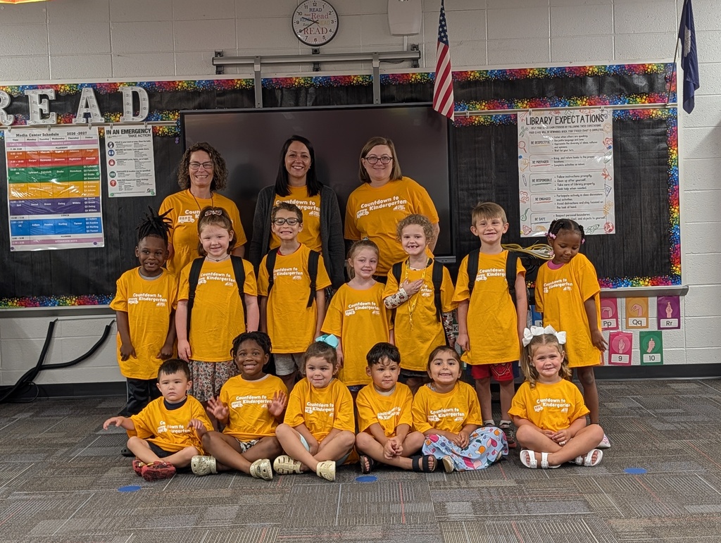 Group of students in yellow shirts and bookbags in library.