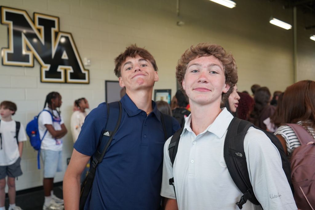 "2 Boys smiling for the camera with students in the background. "