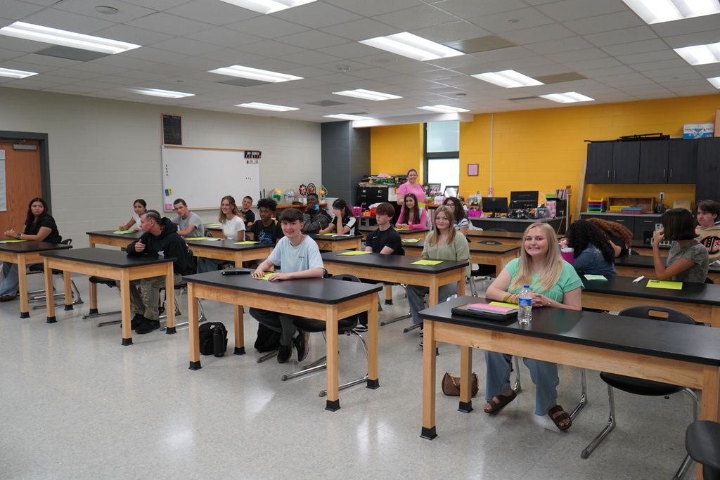 "Teacher with students at desk in classroom."