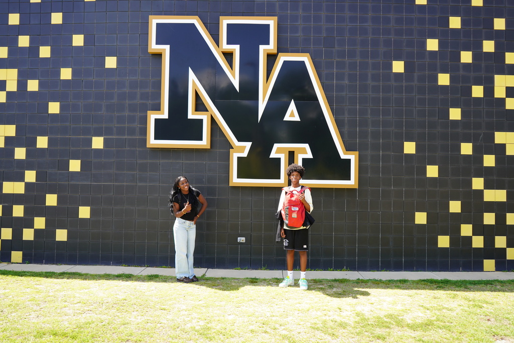 "2 Students standing in front of NA sign."