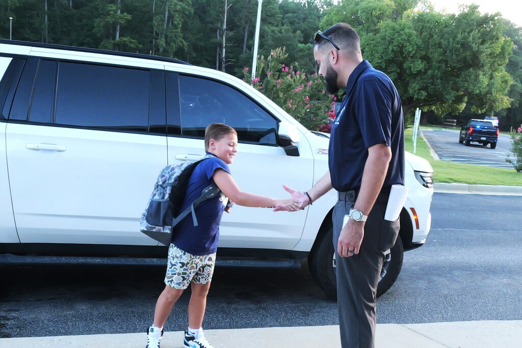 Student shakes hands with an administrator after getting out of the car line.