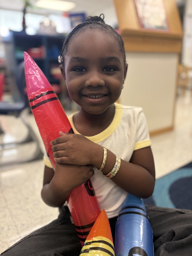 Image of young student holding large crayons and smiling at camera